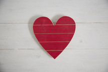 A red wooden heart on a white wood background.