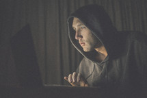 A man in a hooded sweatshirt using a laptop computer.