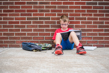 a boy doing his homework leaning against a school building 