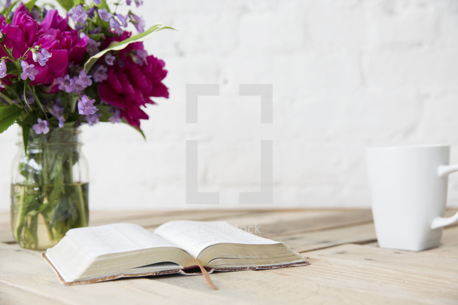 flowers in a vase, open Bible, and coffee mug on a table 