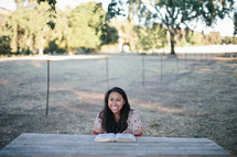 woman reading a Bible outdoors at a picnic table 