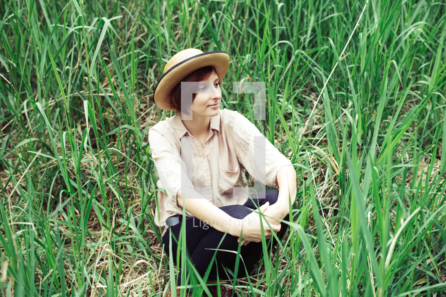 a woman in a straw hat sitting in tall grasses 