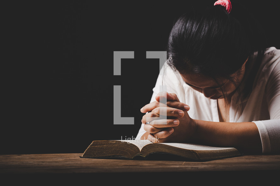 Woman praying with hands on her Bible
