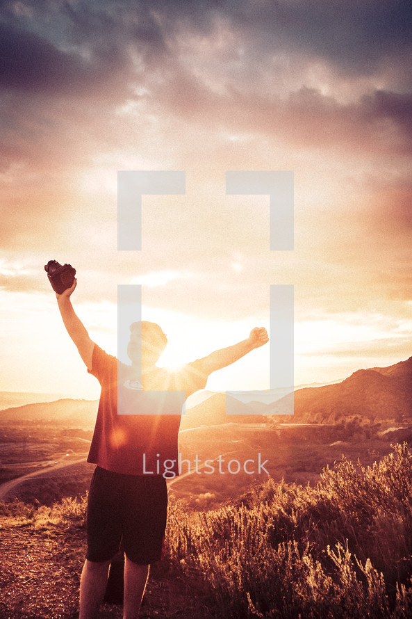 man standing on a mountaintop with raised hands holding a camera 