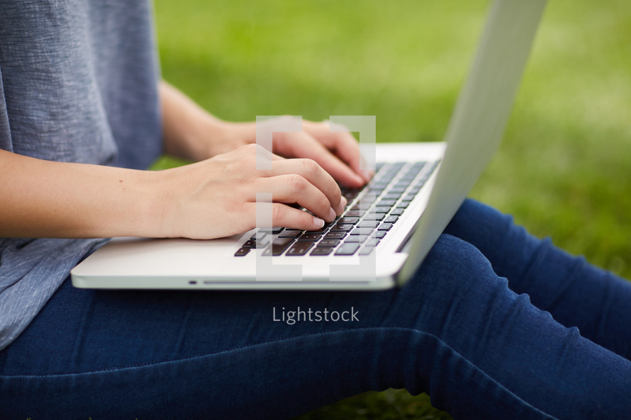 woman sitting in the grass typing on a laptop 