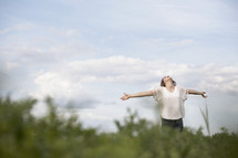 Woman outdoors with arms extended looking up to the heavens.