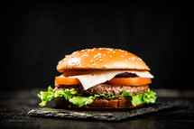 A burger on a stone board on a table. On a black background. High quality photo