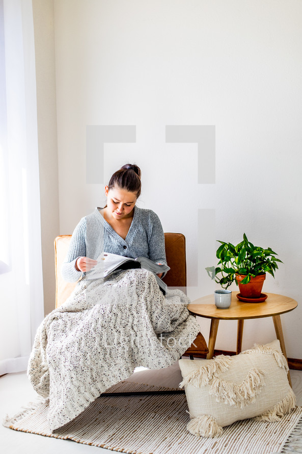 a woman sitting under a blanket reading a Bible 