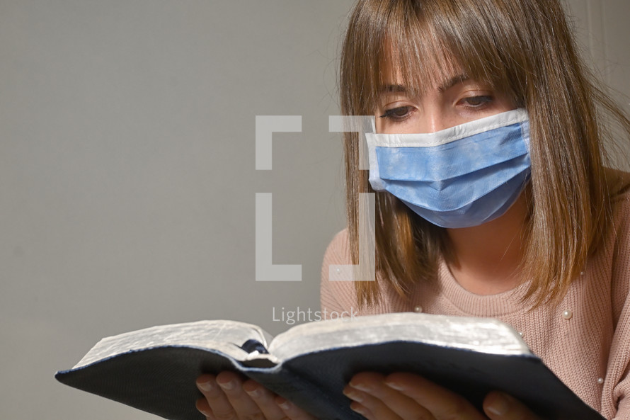 a woman wearing a face mask while reading a Bible 