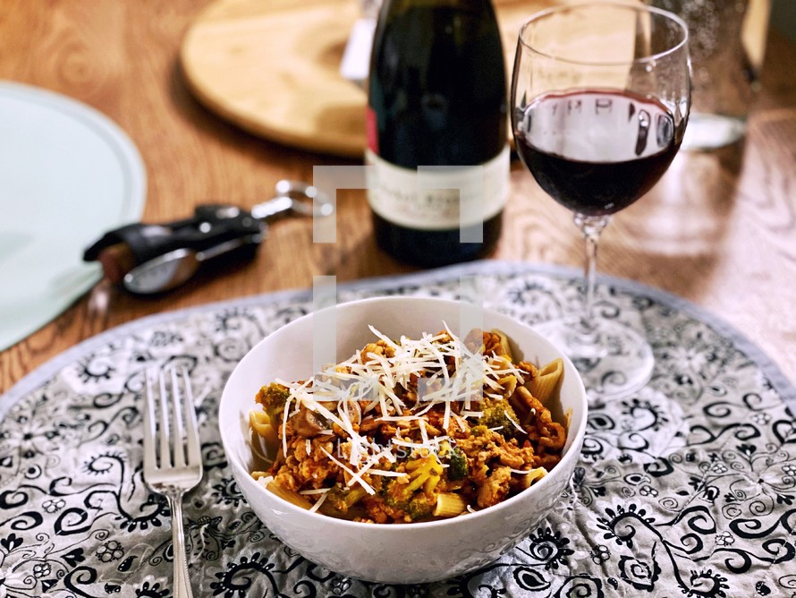 bowl of pasta and a glass of wine at a dinner table 