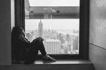 woman looking out a window at city skyscrapers 