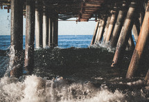 waves crashing into the post of a pier 