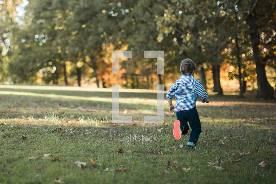 a boy child running outdoors in grass in fall 