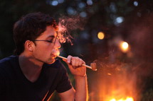 man smoking a pipe by a fire 