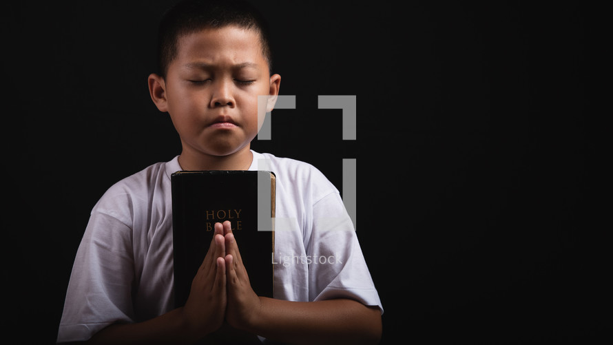 Boy praying to God with a Bible