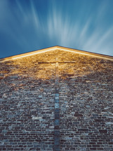 cross on a brick wall under a blue sky 