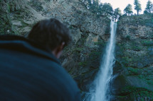 a man looking up at a waterfall 