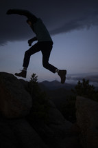silhouette of a man leaping across rocks 