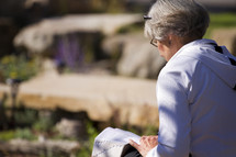 an elderly woman reading a Bible in her lap outdoors 