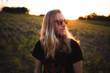 A man with long blonde hair sitting in a field.