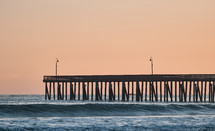 waves and pier under a pink sky 