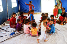 refugee children sitting on the floor in a tent classroom 