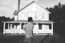 A man stands with hands on hips by a farm house.
