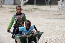 Two boys playing with a wheelbarrow.