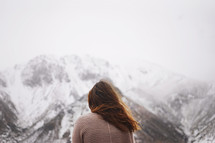 woman looking out at fog over snow capped mountains 