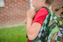 boy walking to school carrying his book bag over his shoulders 