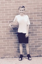 a boy holding a basketball standing against brick wall 