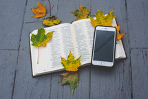 cellphone on the pages of a Bible with fall leaves 