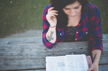 Woman reading the Bible at an outdoor picnic table.