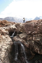 a woman standing on a cliff near a waterfall 