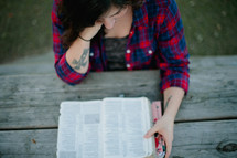 Woman reading the Bible while sitting at a picnic table outside.