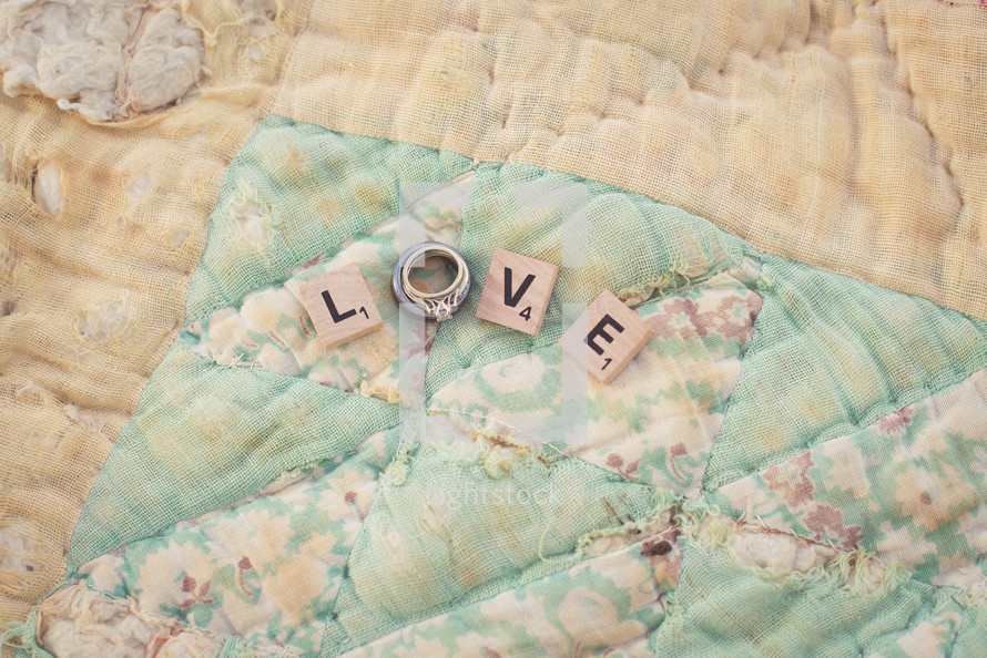 "Love" spelled out by letters and a wedding ring on an old quilt.