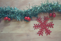 glittery red snowflake ornament and garland on a wood background 