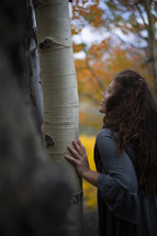 a woman looking up to the top of a fall tree 