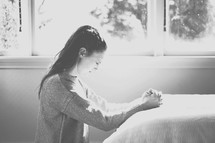 a woman kneeling in prayer by her bedside 