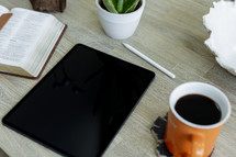 tablet, opened Bible, coffee mug on a table 