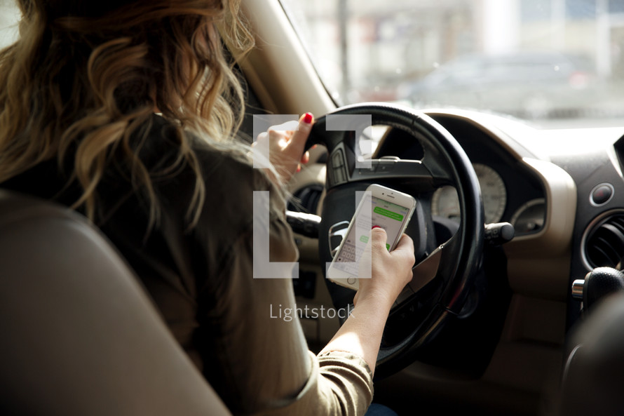A woman texting on her phone while driving a car.