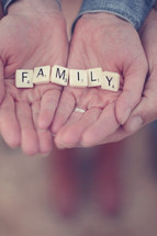 Hands holding letter tiles spelling "family."