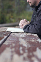man praying over a Bible at a picnic table 