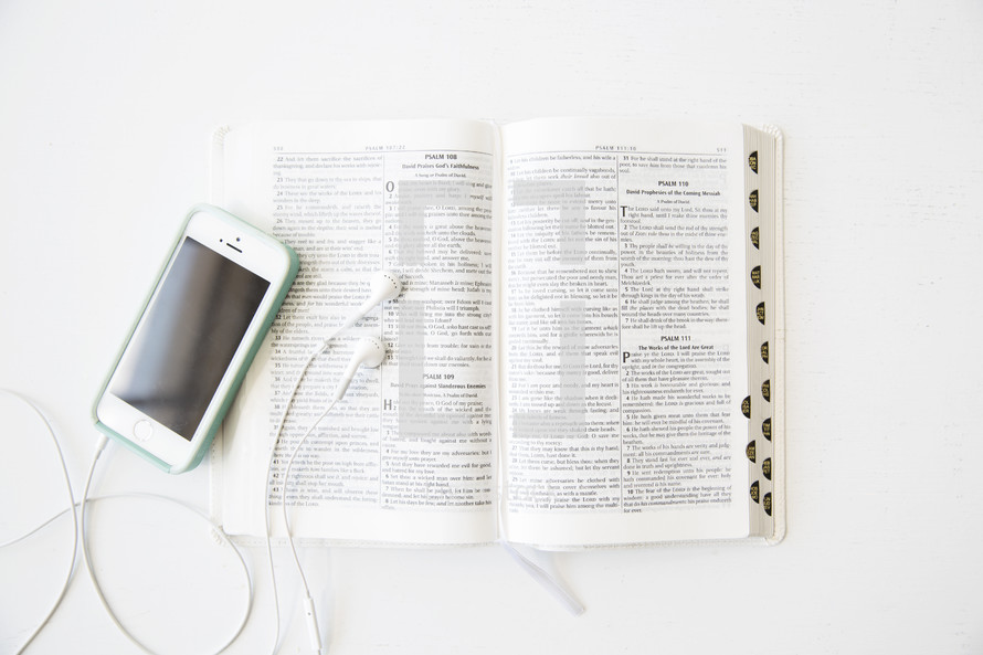 A cell phone and ear phones on an open Bible.