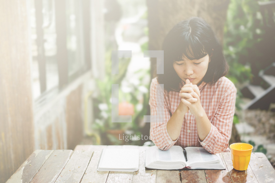 a woman praying sitting at a table with an open Bible 