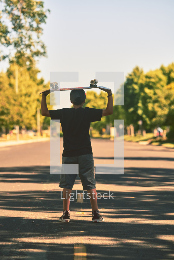 boy holding a skateboard over his head 