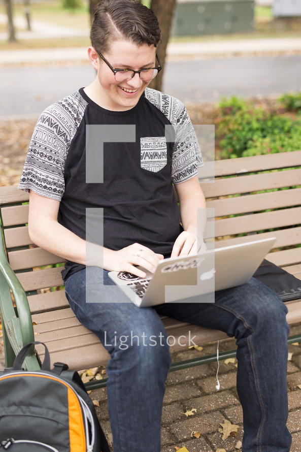 a college student sitting on bench with his laptop 