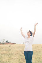Woman standing in a field with arms raised in praise.