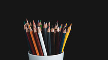 colored pencils in white cup on a black background
