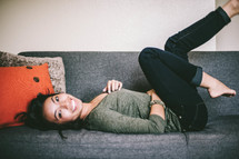 Young woman laing down on a couch, kicking legs up